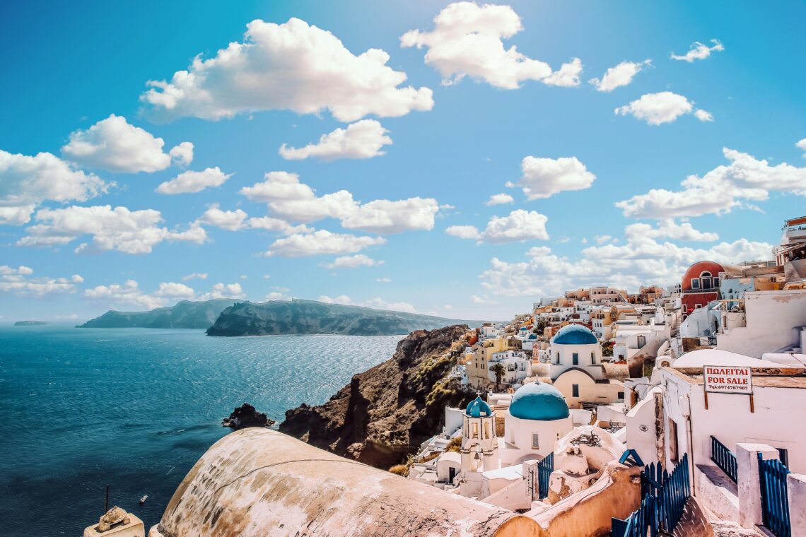 white-concrete-house-near-body-of-water-under-white-and-blue-cloudy-sky-greece